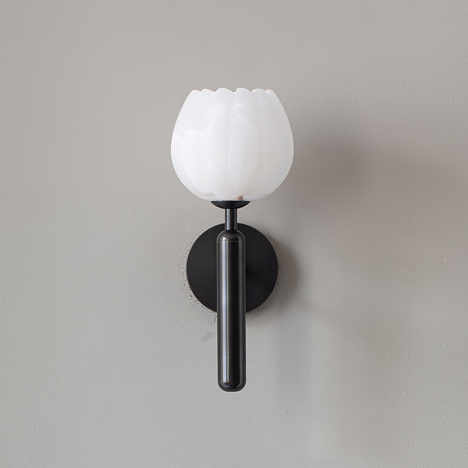 Unlit Clérachic alabaster wall sconce in black on a plain wall, showing the white stone cup, round plate and baton.
