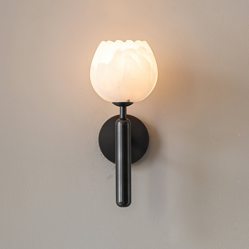Black Clérachic alabaster wall sconce switched on, the stone cup warm gold and a halo of light spread across the wall.