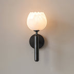 Black Clérachic alabaster wall sconce switched on, the stone cup warm gold and a halo of light spread across the wall.