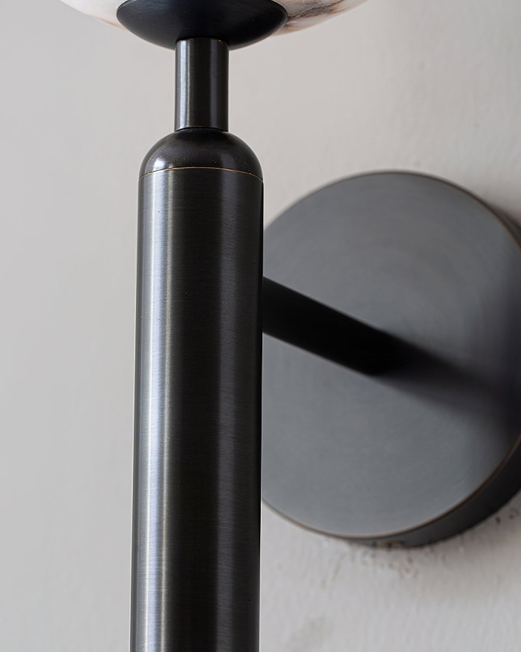 Detail of the Clérachic alabaster wall sconce in black, the gunmetal baton meeting the arm and round wall plate.