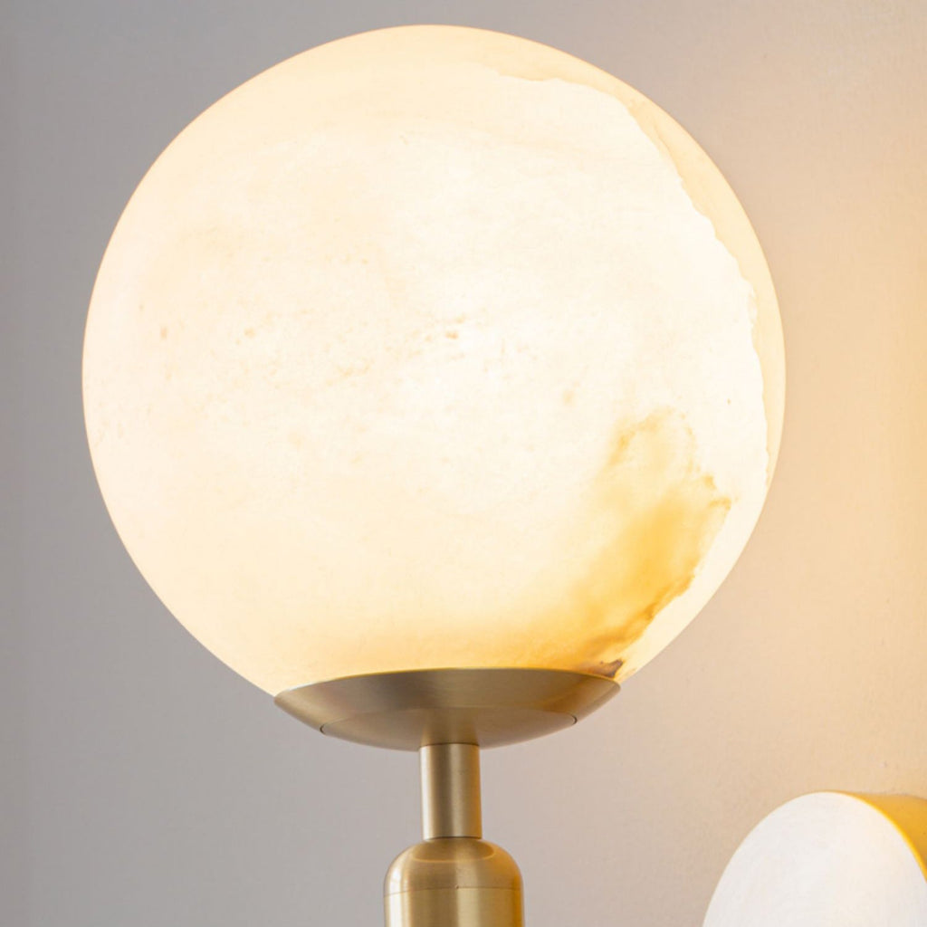 Close-up of the lit globe shade on the Clérachic alabaster wall sconce, amber veining drifting through the stone.
