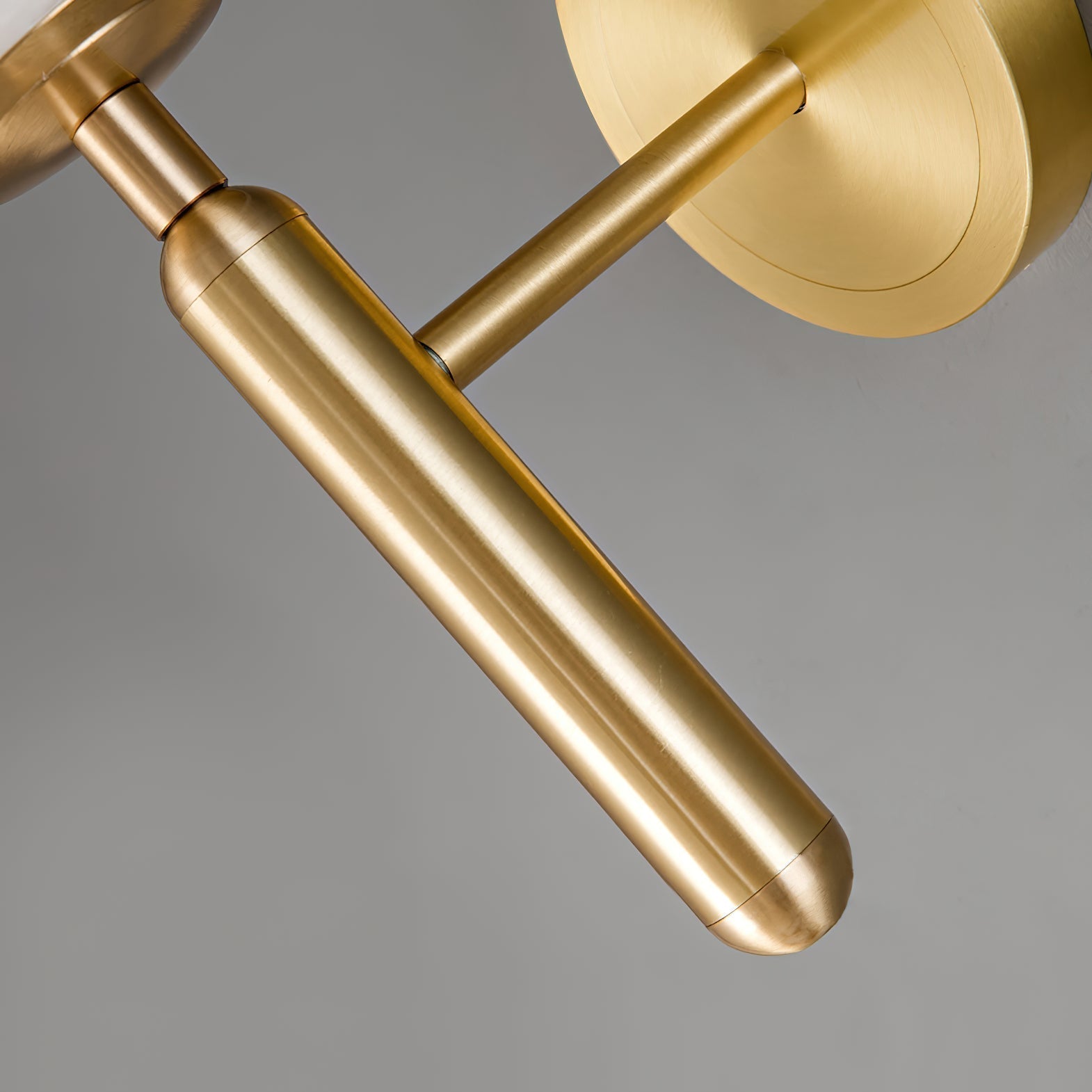 Detail of the brushed brass arm, rounded baton and wall plate on the Clérachic alabaster wall sconce, seen from below.