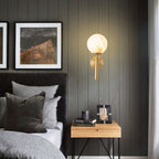Brass Clérachic alabaster wall sconce lit on a dark timber-panelled bedroom wall above a nightstand stacked with books.