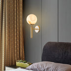 Brass Clérachic alabaster wall sconce glowing beside a gold woven curtain in a grey panelled bedroom, succulents below.