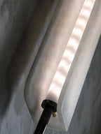 Angled close-up of the Clérachic Alabaster Wall Sconce lit, the LED strip visible in the gap where the two stone plates overlap.