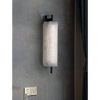 Clérachic Alabaster Wall Sconce lit on a grey concrete wall beside a curtain, sitting shallow enough to clear a bedside table.