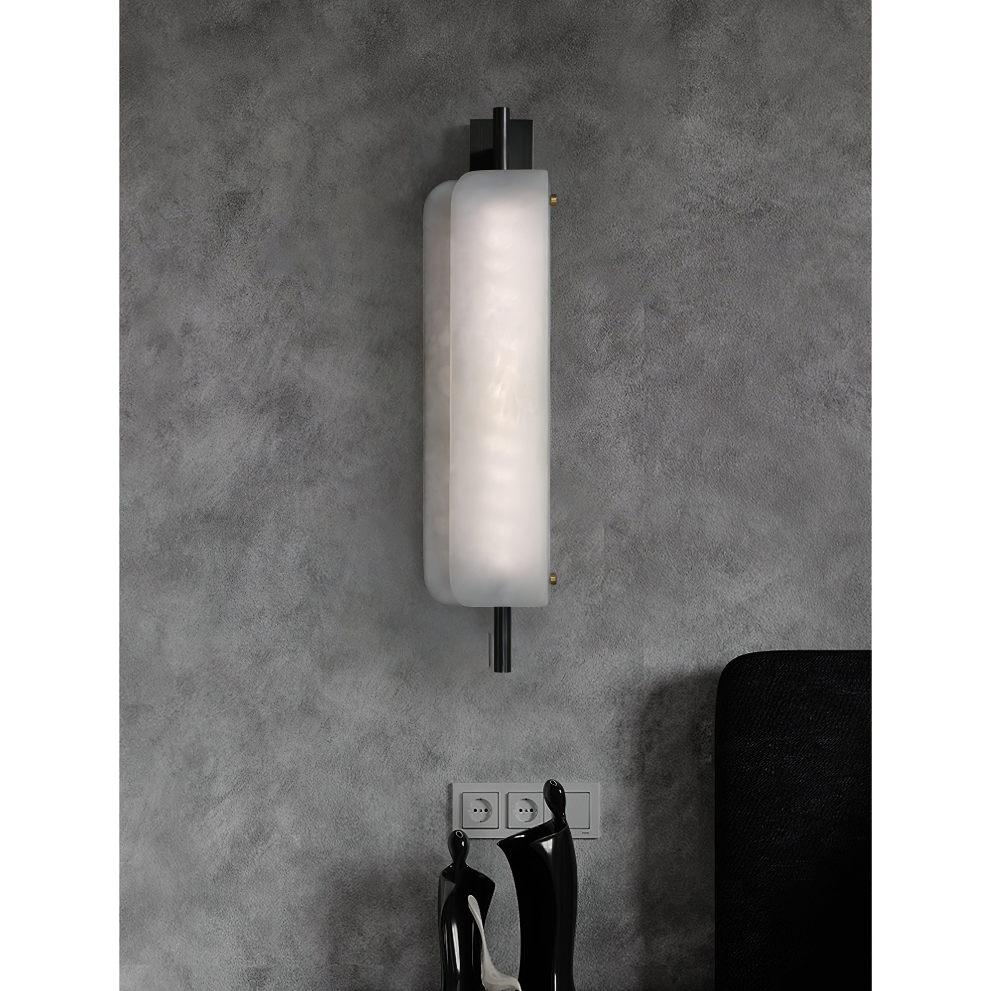 Clérachic Alabaster Wall Sconce lit above a pair of dark figurines, the offset plates sending light up the wall and down over what sits below.