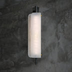 Clérachic Alabaster Wall Sconce lit against a dark concrete wall, the alabaster face even and bright from the rod above to the rod below.