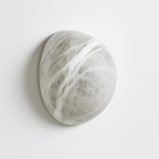 Clérachic pebble-shaped alabaster wall sconce in soft white with grey veining, mounted flat on a pale studio wall.