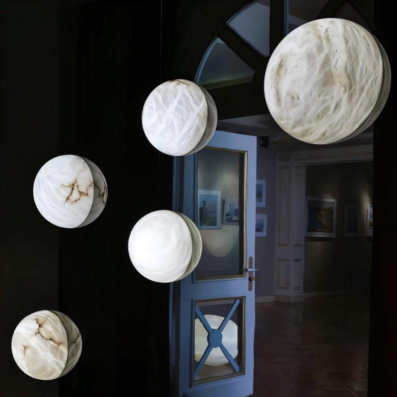 Clérachic several round white alabaster wall lights in different sizes, glowing against a dark room beside an open blue door.