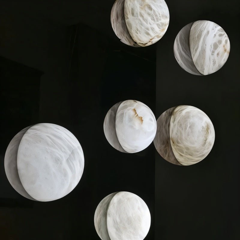 Clérachic cluster of round veined alabaster wall lights in assorted sizes, glowing softly against a dark wall.