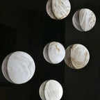 Clérachic cluster of round veined alabaster wall lights in assorted sizes, glowing softly against a dark wall.