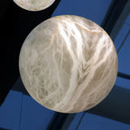 Clérachic close up of a large rounded alabaster light with white and amber veining, seen against a dark and blue backdrop.