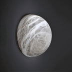Clérachic pebble-shaped alabaster wall sconce with grey and white veining, mounted on a dark charcoal wall in the studio.