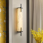 A lit Clérachic alabaster wall light with a black frame sits beside floral yellow curtains and a vase of yellow flowers.