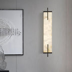 An unlit Clérachic alabaster wall light with black bars hangs on a grey panelled wall beside a framed calligraphy print.