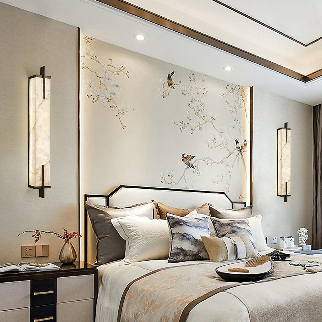 A pair of Clérachic alabaster wall lights flank a bed against a wall painted with birds and blossom branches.