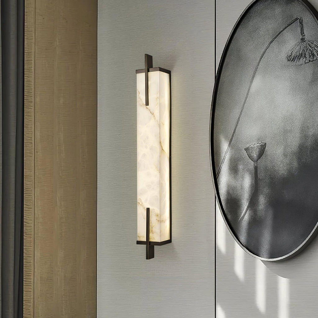 A lit Clérachic alabaster wall light with a black frame hangs on a pale wall next to a large round ink-wash painting of a lotus.
