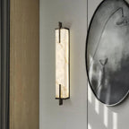 A lit Clérachic alabaster wall light with a black frame hangs on a pale wall next to a large round ink-wash painting of a lotus.