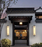 A pair of lit Clérachic alabaster wall lights flank a dark timber gateway on a white wall in a courtyard-style entrance at dusk.
