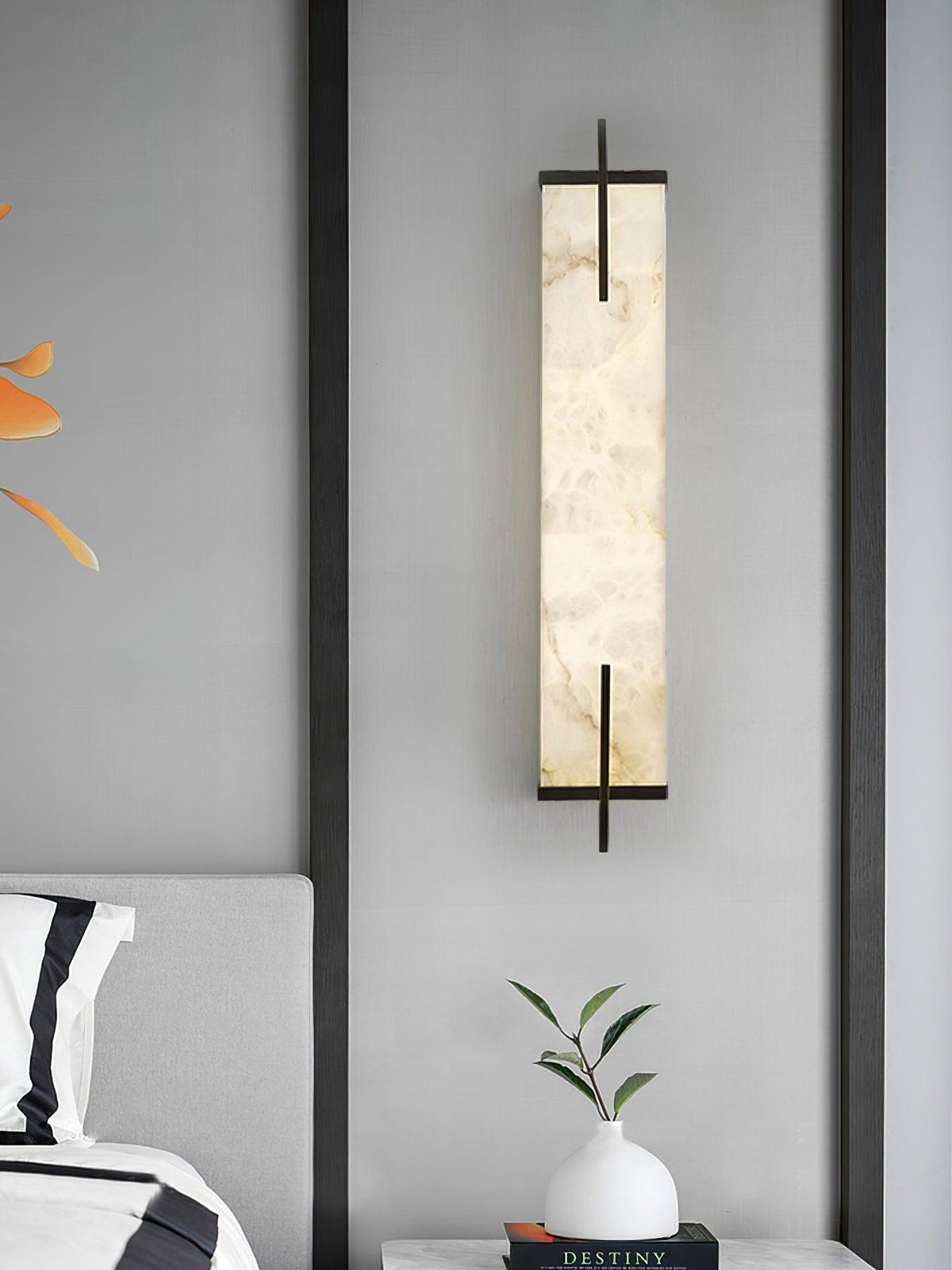 Closer view of this Clérachic alabaster wall light on a grey wall between dark pilasters, with a bedside vase and a book below.
