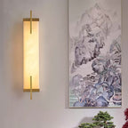 A Clérachic alabaster wall light with a gold-toned frame glows beside a large mountain landscape painting and a bonsai on a console.