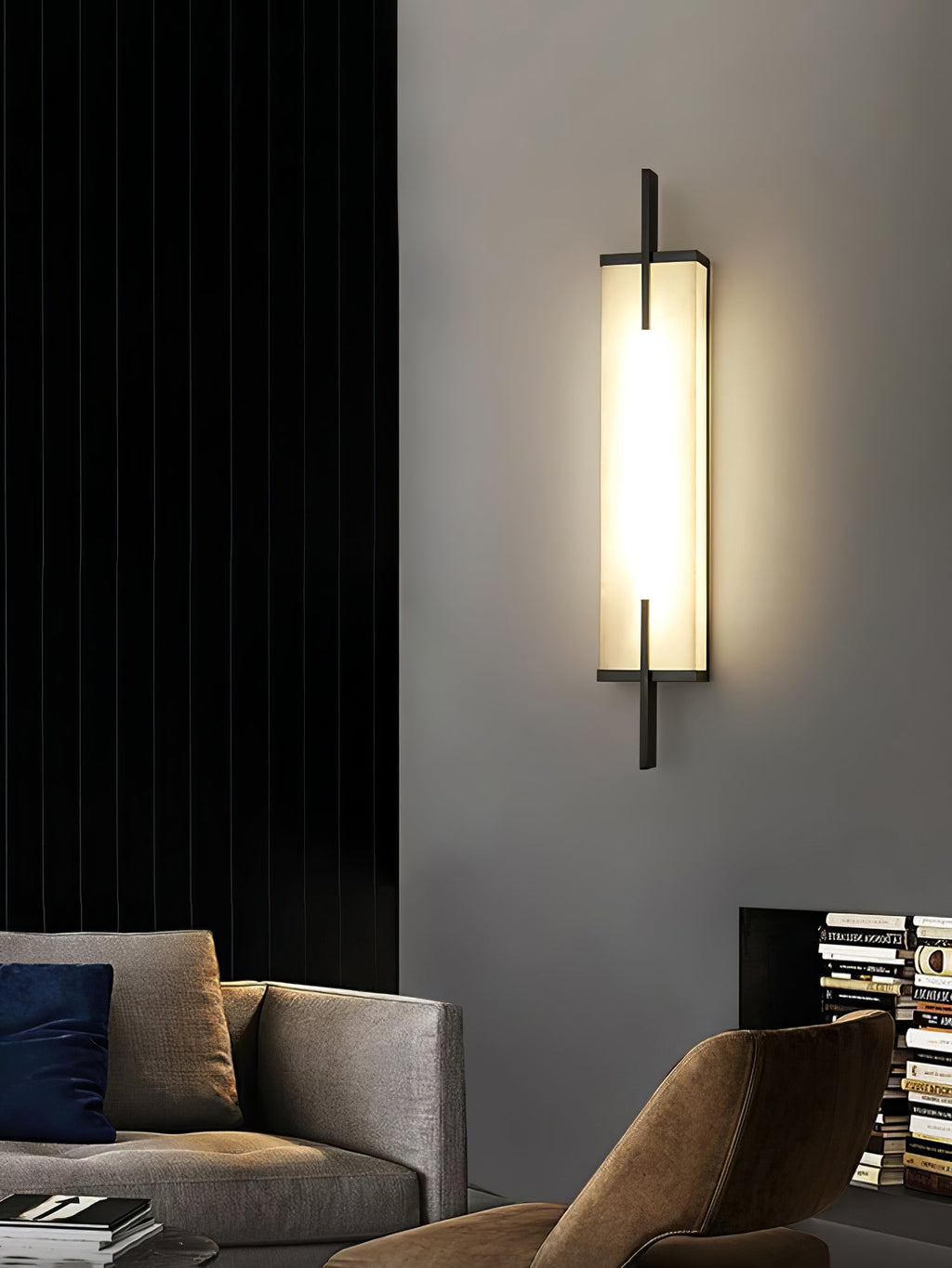 A lit Clérachic alabaster wall light with a black frame hangs beside a black curtain above a tan sofa and an armchair.