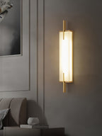 A Clérachic wall light with a gold-toned frame and a glowing alabaster panel hangs on a panelled grey wall above a sofa.