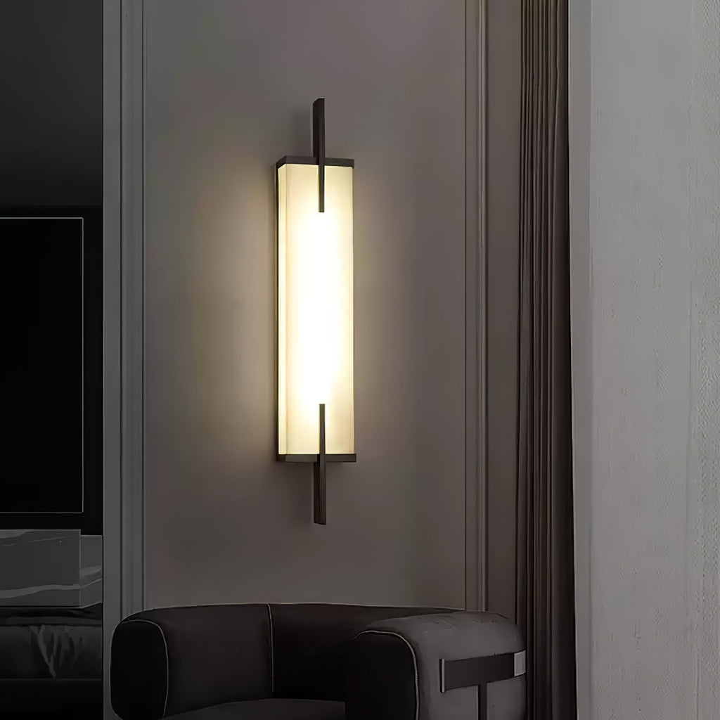 A lit Clérachic alabaster wall light with a black frame glows on a grey wall beside a curtain, above a dark leather armchair.