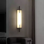 A lit Clérachic alabaster wall light with a black frame glows on a grey wall beside a curtain, above a dark leather armchair.