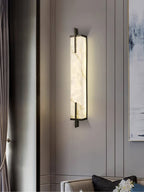 A Clérachic alabaster wall light with a black frame glows beside a long grey curtain and a pale abstract painting.