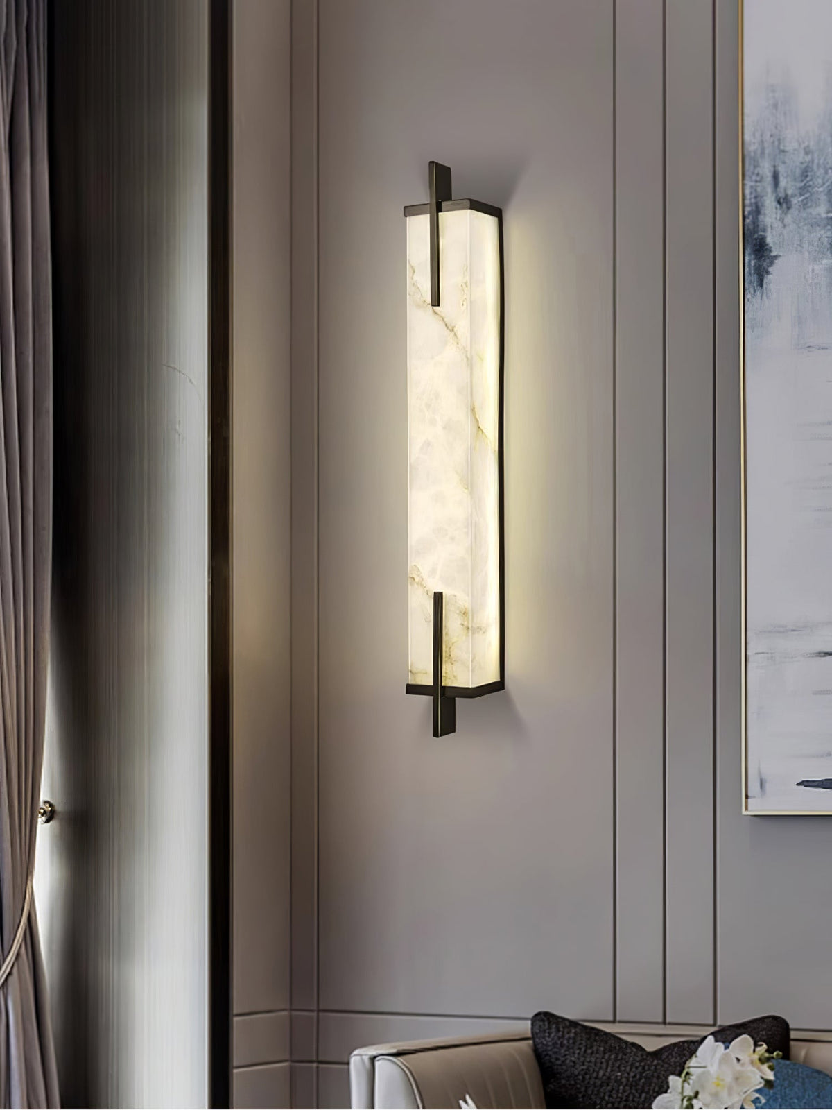 A Clérachic alabaster wall light with a black frame glows beside a long grey curtain and a pale abstract painting.