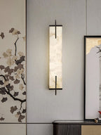 A Clérachic alabaster wall light with a black frame hangs against a ginkgo-leaf wall panel, beside a framed landscape and a dark console.