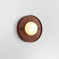 Studio shot of the round Clérachic Alabaster Wall Sconce, the stone globe glowing softly against warm walnut grain.
