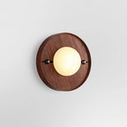 Studio shot of the round Clérachic Alabaster Wall Sconce, the stone globe glowing softly against warm walnut grain.