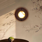 Close view of the lit Clérachic Alabaster Wall Sconce, amber veining running across the glowing stone in its round walnut surround.