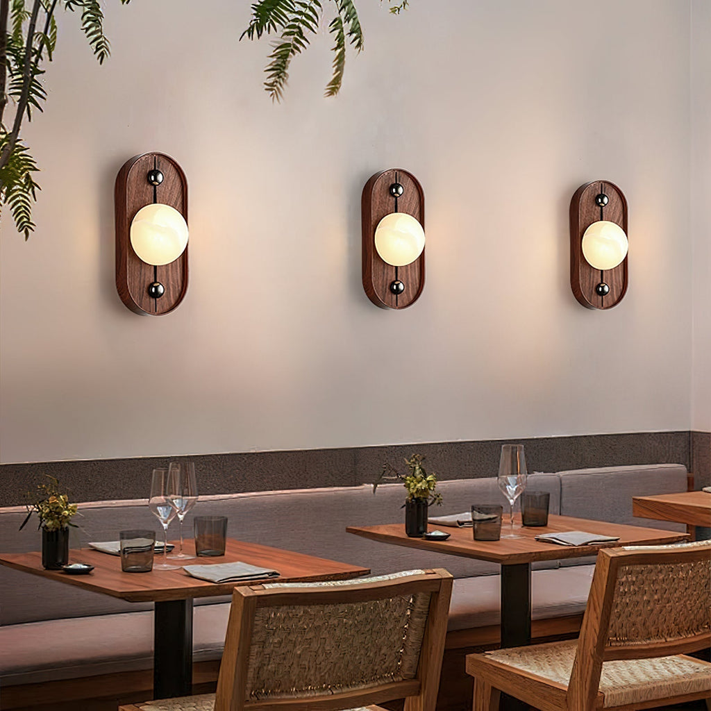 Three oval Clérachic Alabaster Wall Sconce fittings in a row above restaurant banquette seating, each washing the wall with warm light.