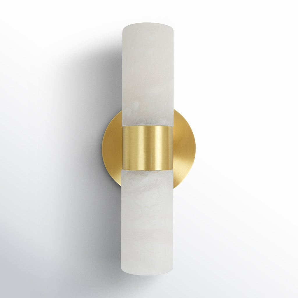 The Clérachic Alight sconce seen from the front corner, round brass backplate flush to the wall behind the stone.