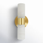 The Clérachic Alight sconce seen from the front corner, round brass backplate flush to the wall behind the stone.