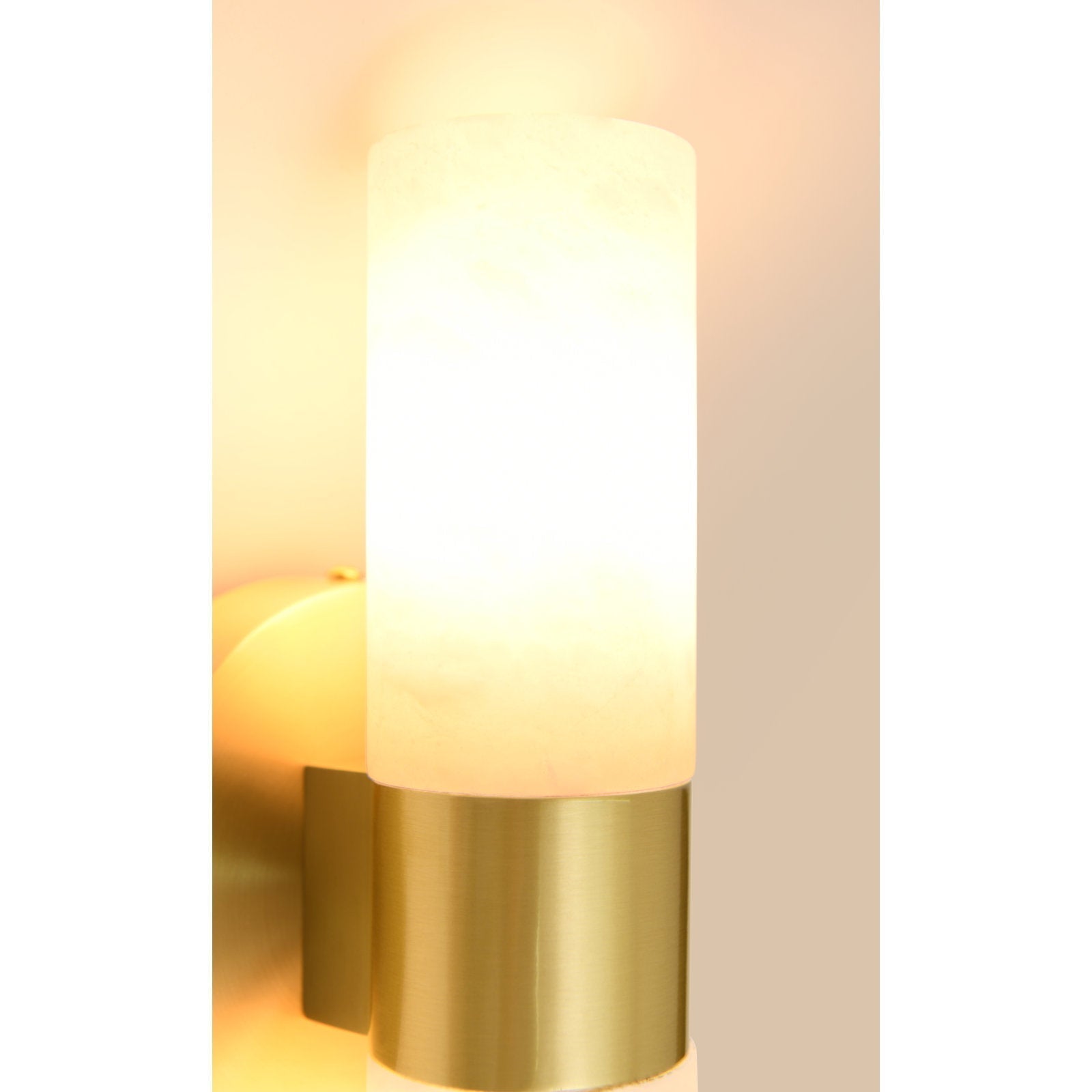 The Clérachic Alight sconce lit, warm light glowing through the alabaster while the brass collar stays bright.
