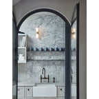 The Clérachic Alight sconces lighting a marble-lined scullery, mounted either side of shelves above a deep sink.