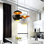 A black and a white Clérachic pendant with gold interiors hang above a marble kitchen island beside tall windows.