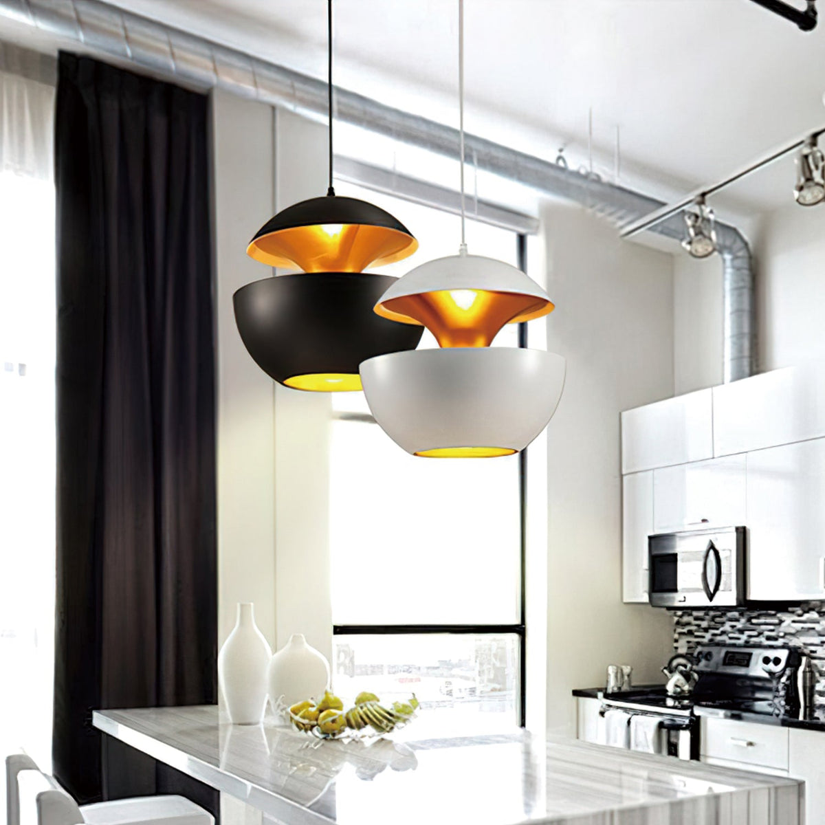 A black and a white Clérachic pendant with gold interiors hang above a marble kitchen island beside tall windows.