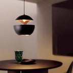 This Clérachic black pendant glows above a dark round table with a green glass vase, its gold interior showing at the gap.