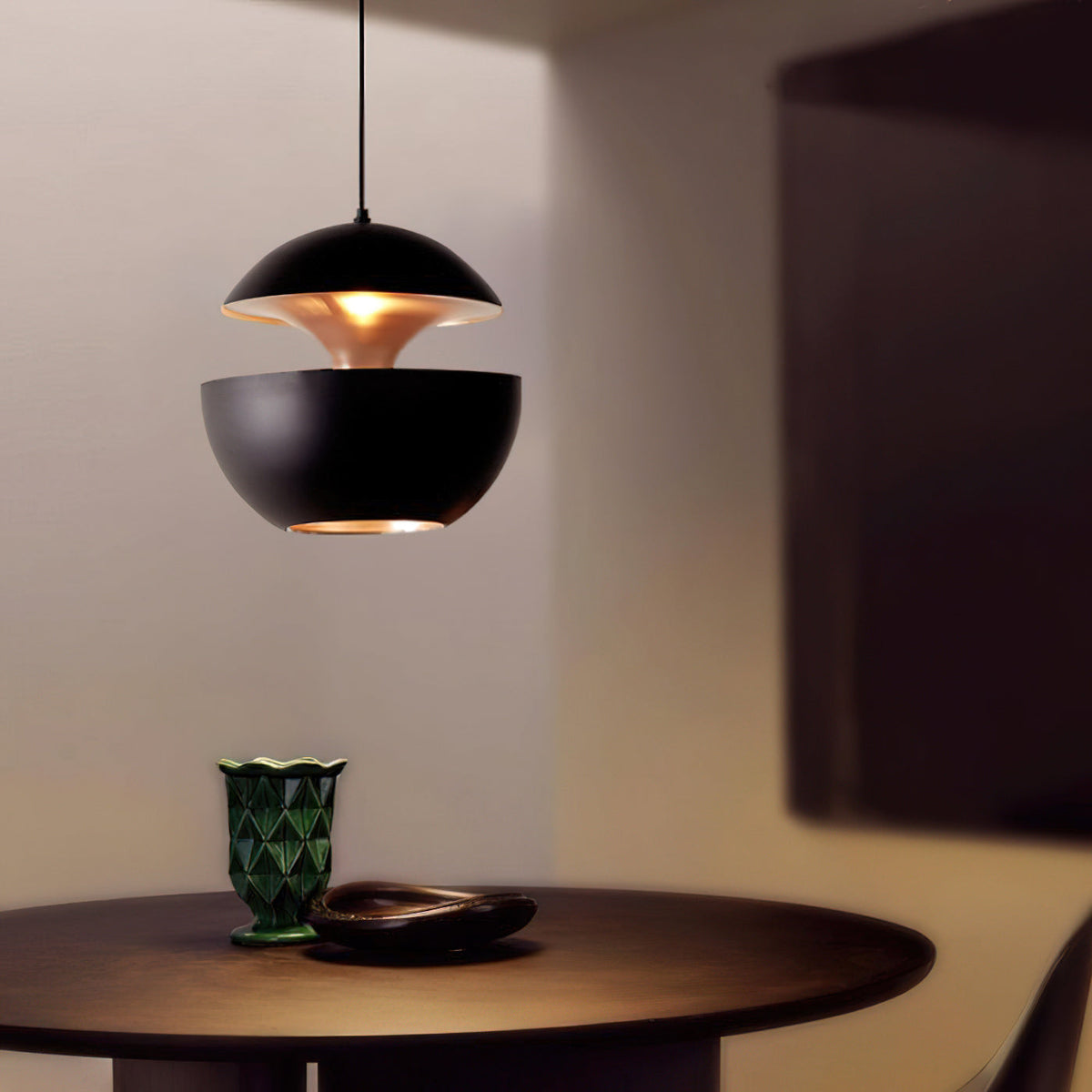 This Clérachic black pendant glows above a dark round table with a green glass vase, its gold interior showing at the gap.
