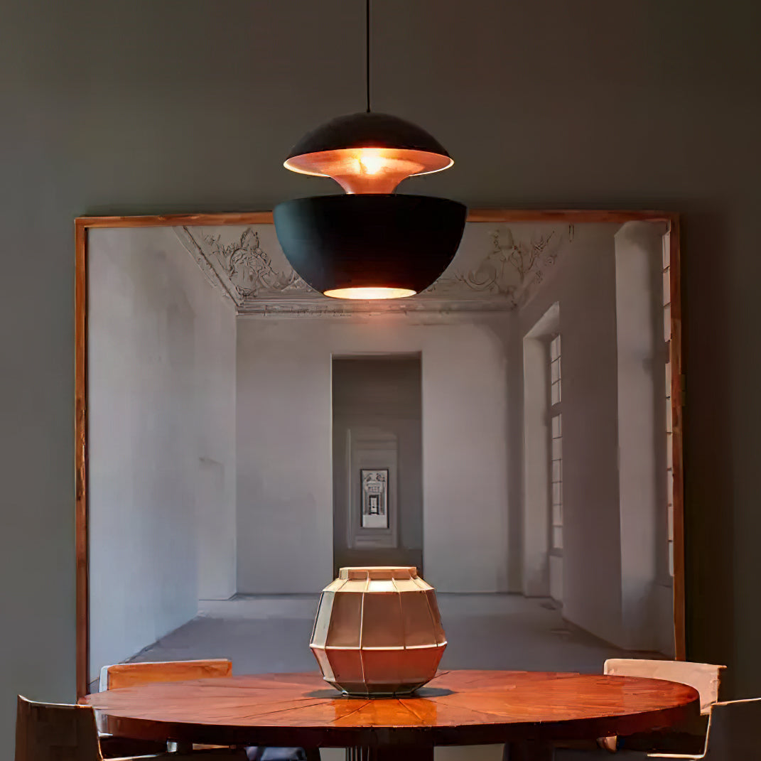 Black Clérachic pendant with gold interior hung over a round wooden table in front of a large framed picture of a hall.