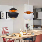 Black and white bowl pendants with gold interiors hang over a pale wood dining table in a bright kitchen, from Clérachic.