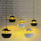 Five black and white Clérachic pendants at different heights glow gold against a white brick wall.