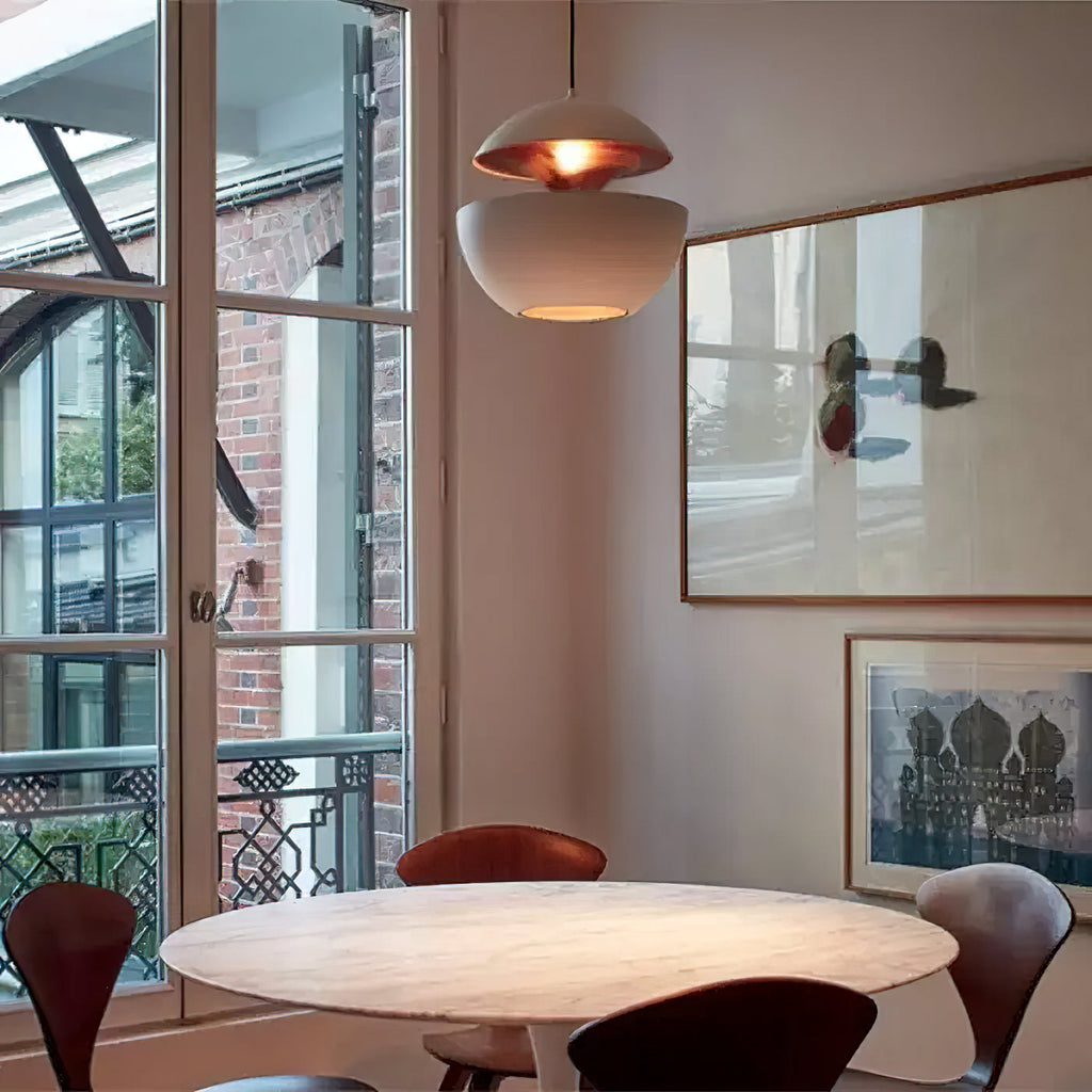 White pendant with a copper-gold interior hung beside tall windows over a round white table, a lamp from Clérachic.