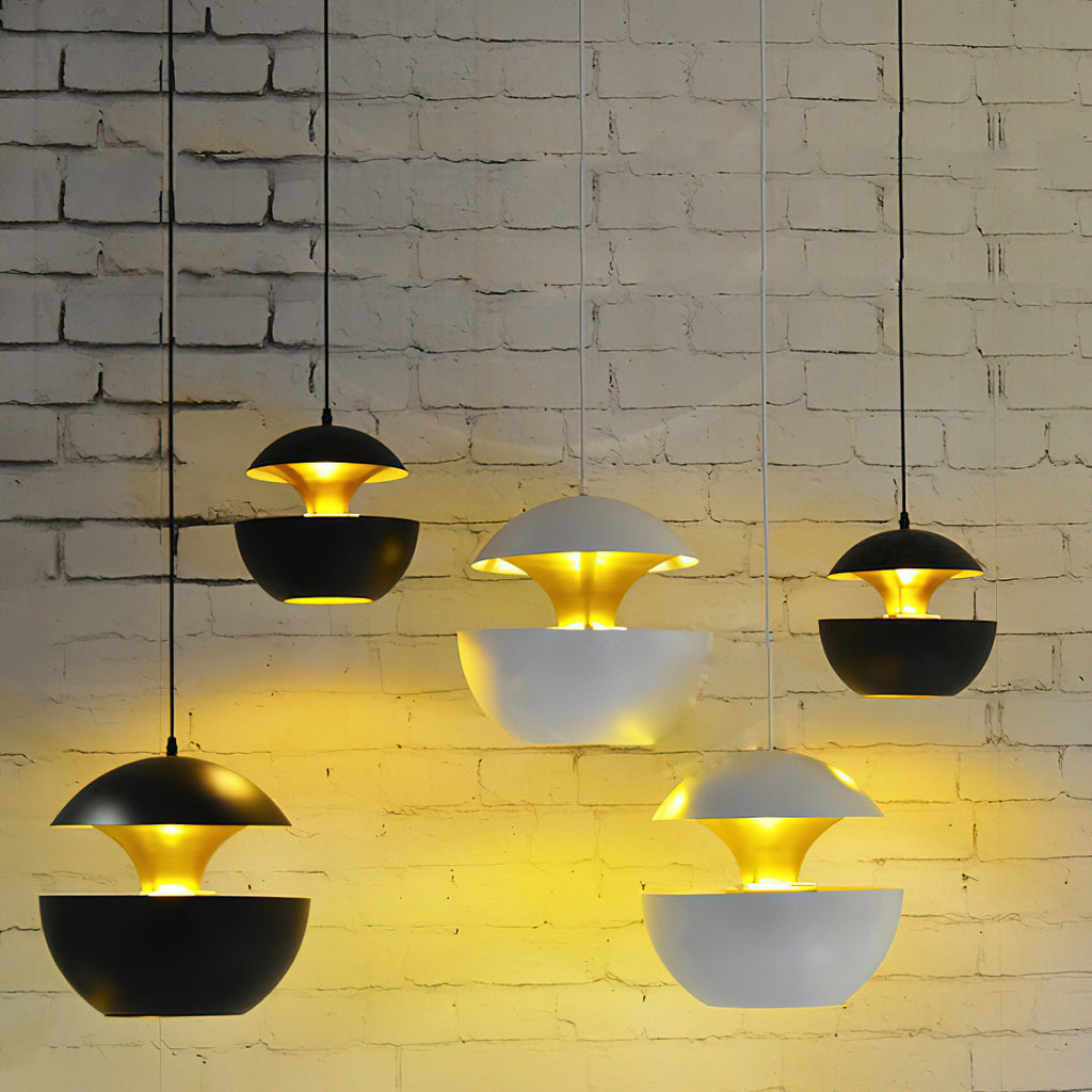 Cluster of black and white Clérachic pendants lit at staggered heights, warm light washing over a painted brick wall.